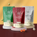Three stand-up pouches of Vayu Farms Roasted Makhanas — Fresh Mint (green), Peri Peri (red), Himalayan Salt & Pepper (silver) — on pastel pedestals against a warm gradient background.
